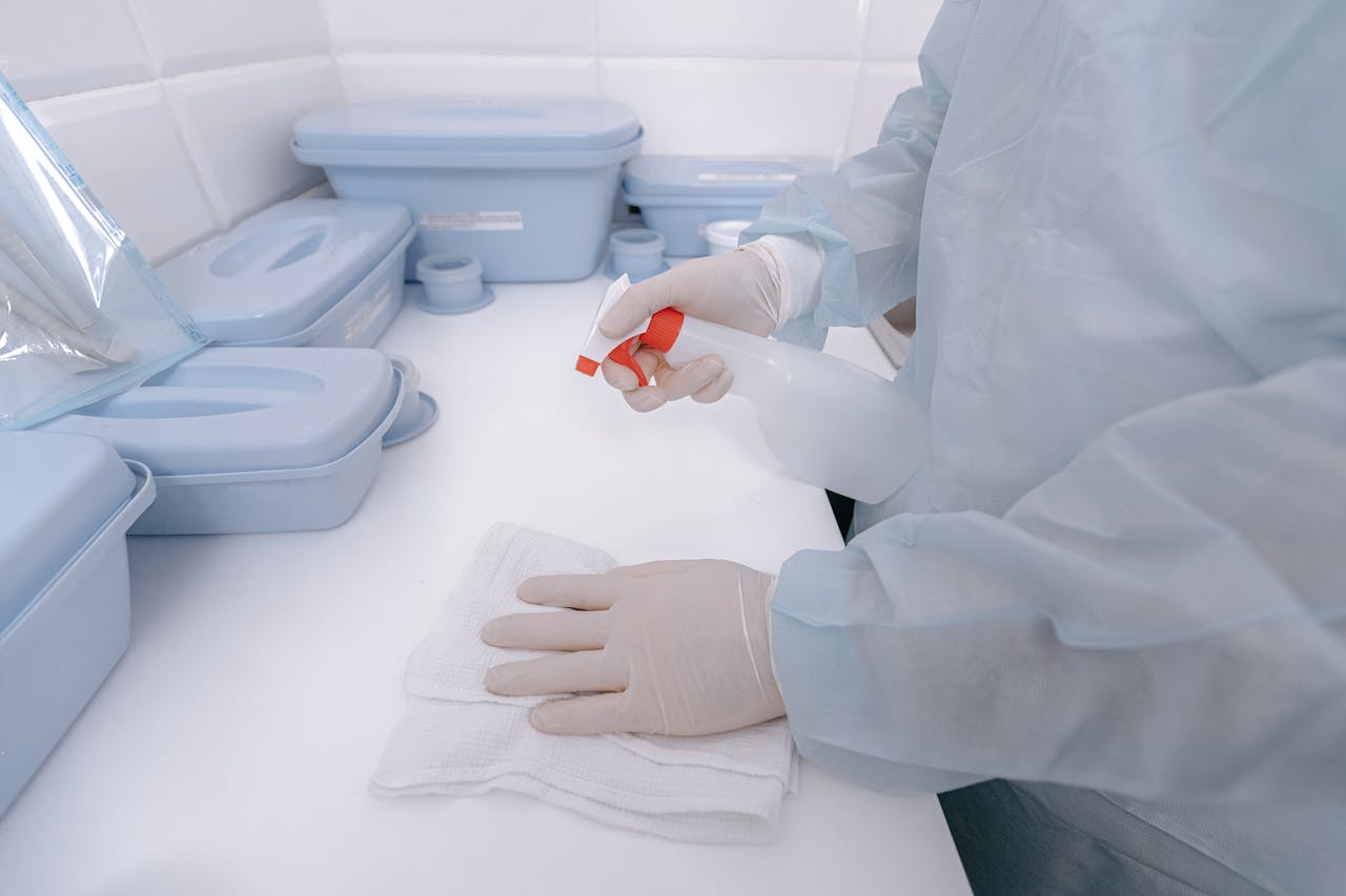 services-04 A healthcare worker wearing gloves sanitizes a surface with a spray bottle in a medical setting.