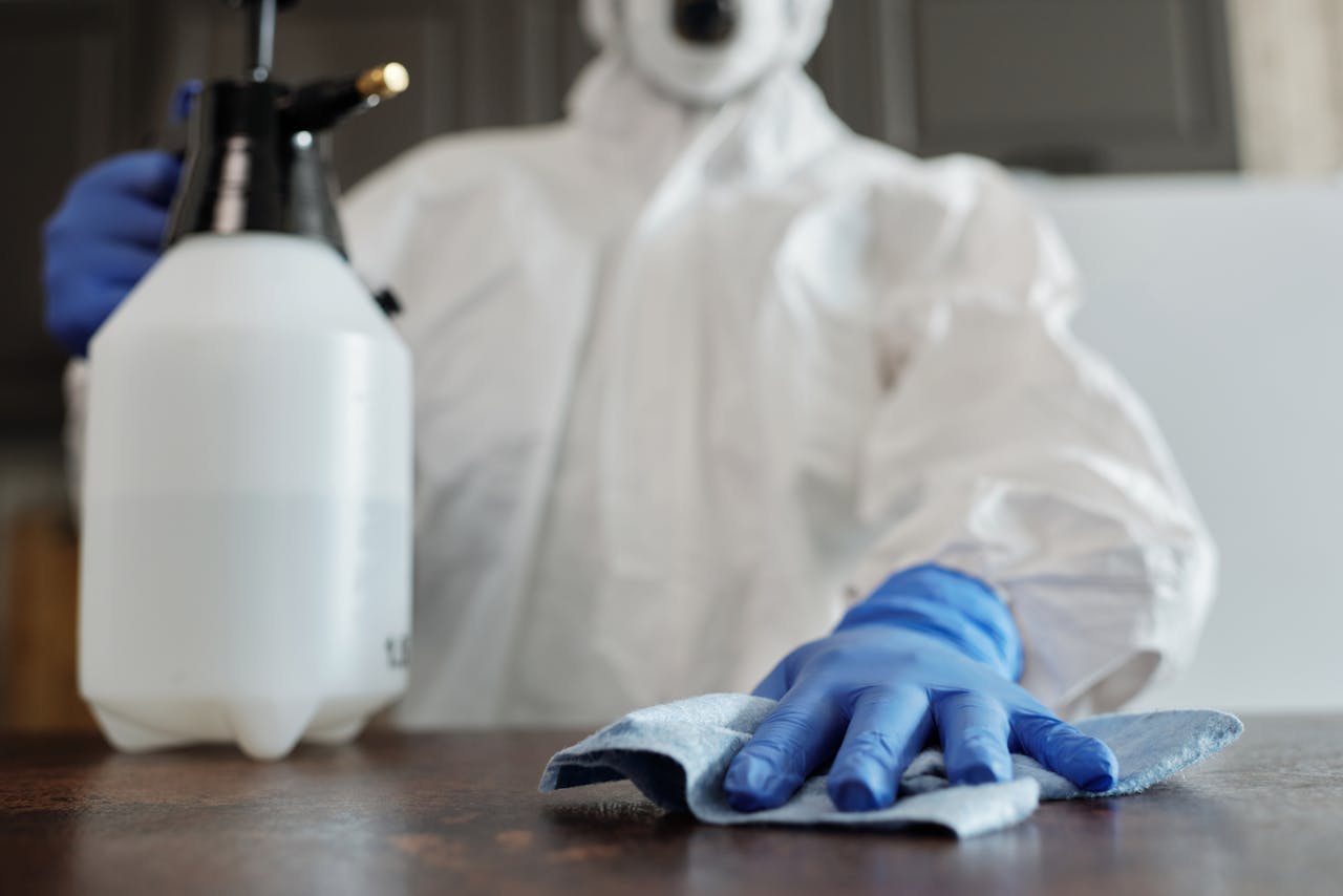 hero-img Close-up of a person in protective gear disinfecting a surface, emphasizing hygiene and cleanliness.